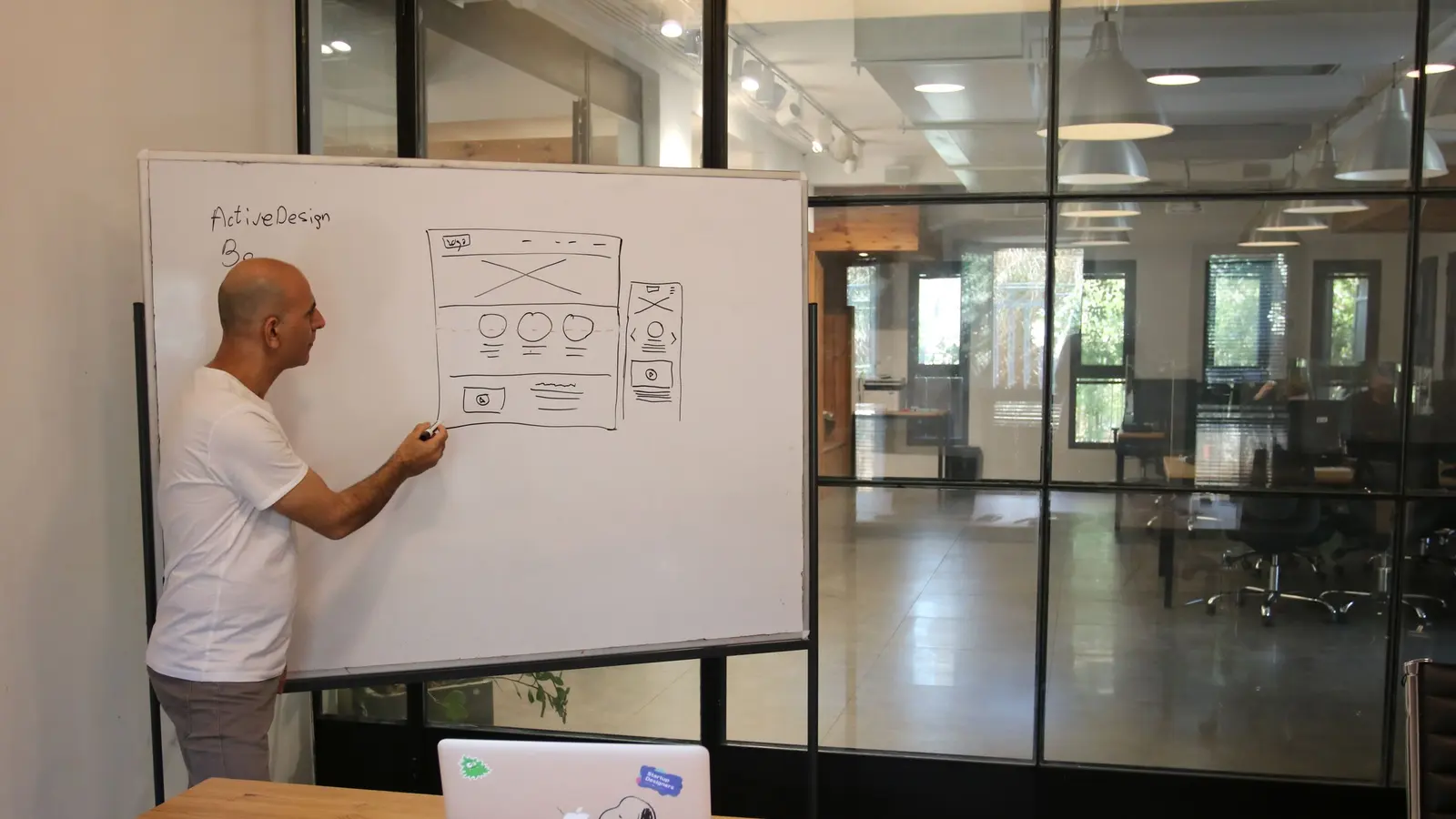 A designer sketching a website layout on a whiteboard in an office