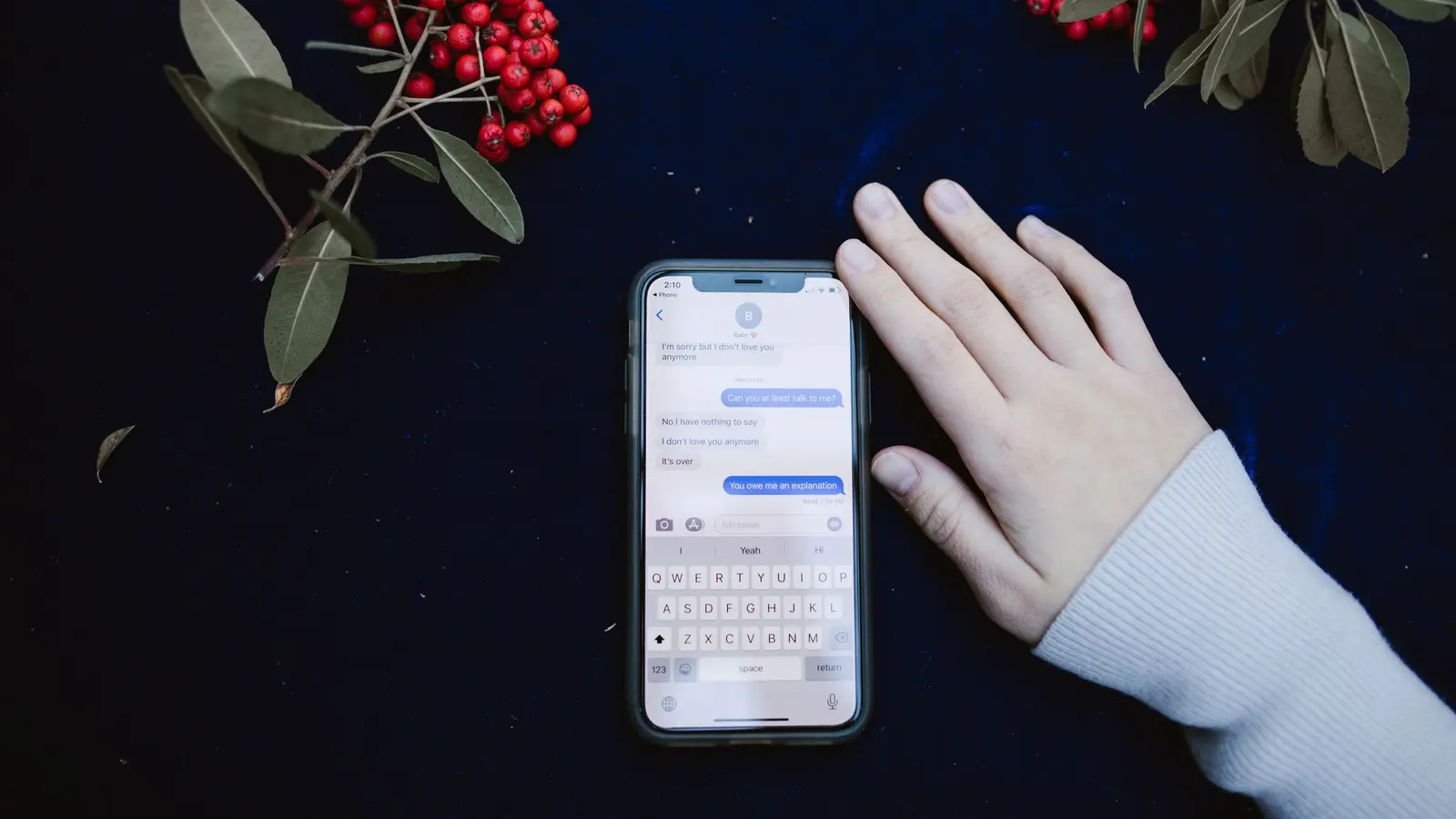 A hand resting on a dark surface beside a phone showing a text message conversation