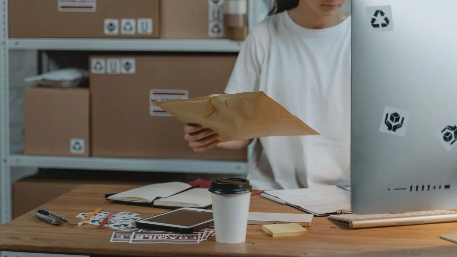 An online store owner packing an order at a desk in front of stock shelves