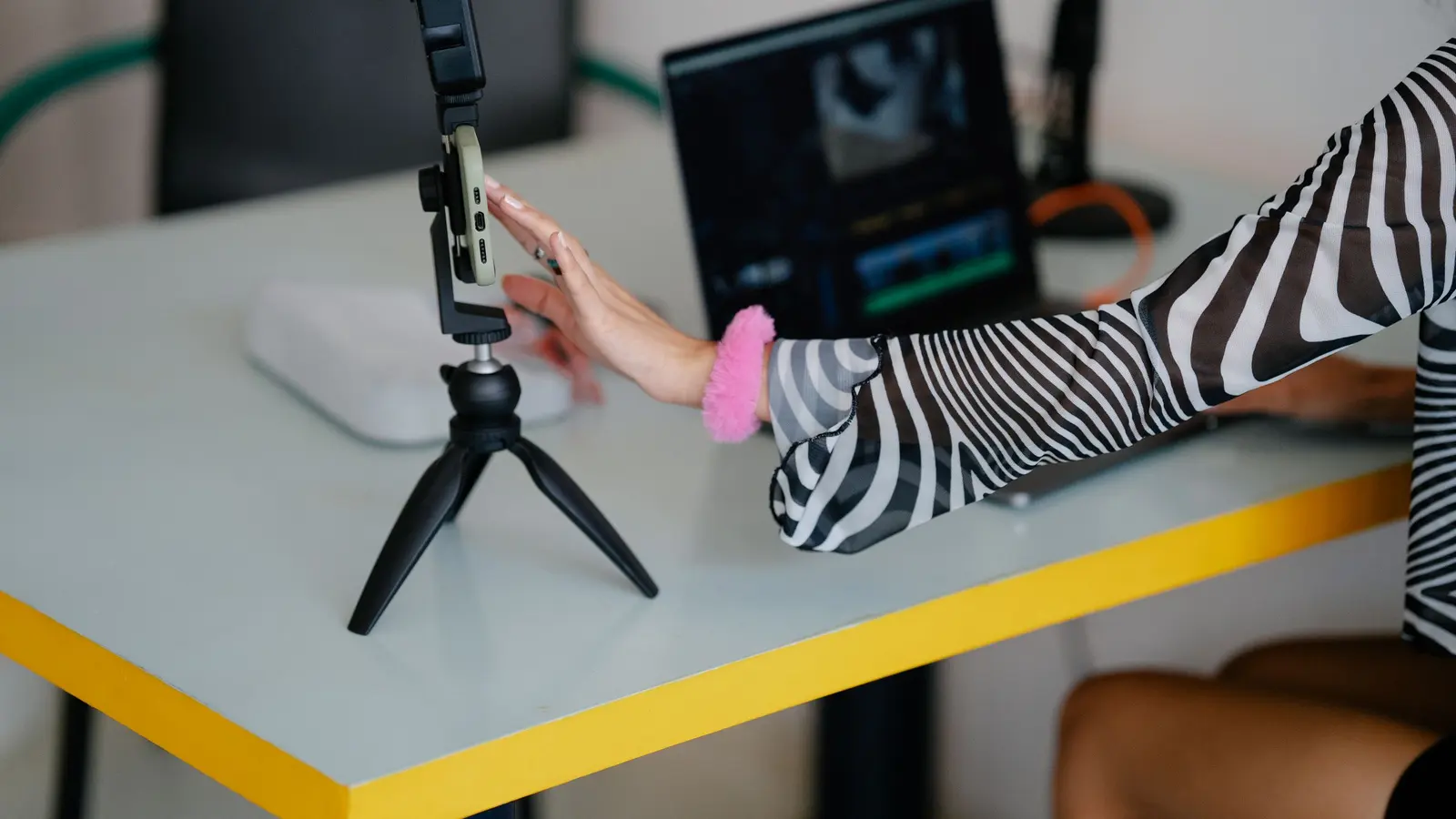 A person setting up a phone on a small tripod beside a laptop to record a video