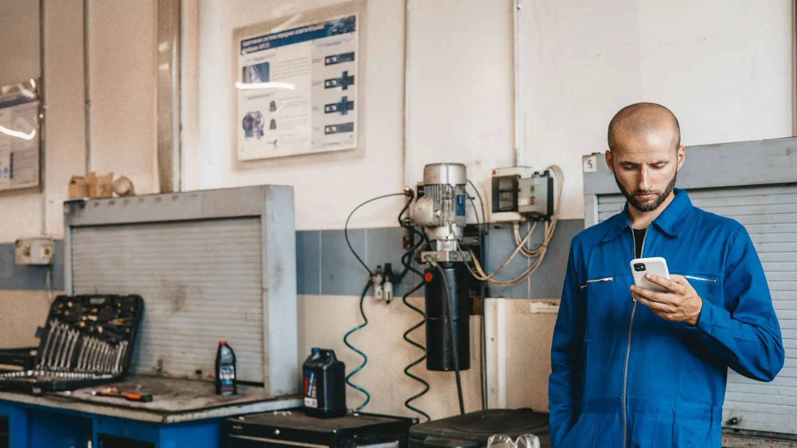 A mechanic in blue coveralls checking his phone inside a workshop