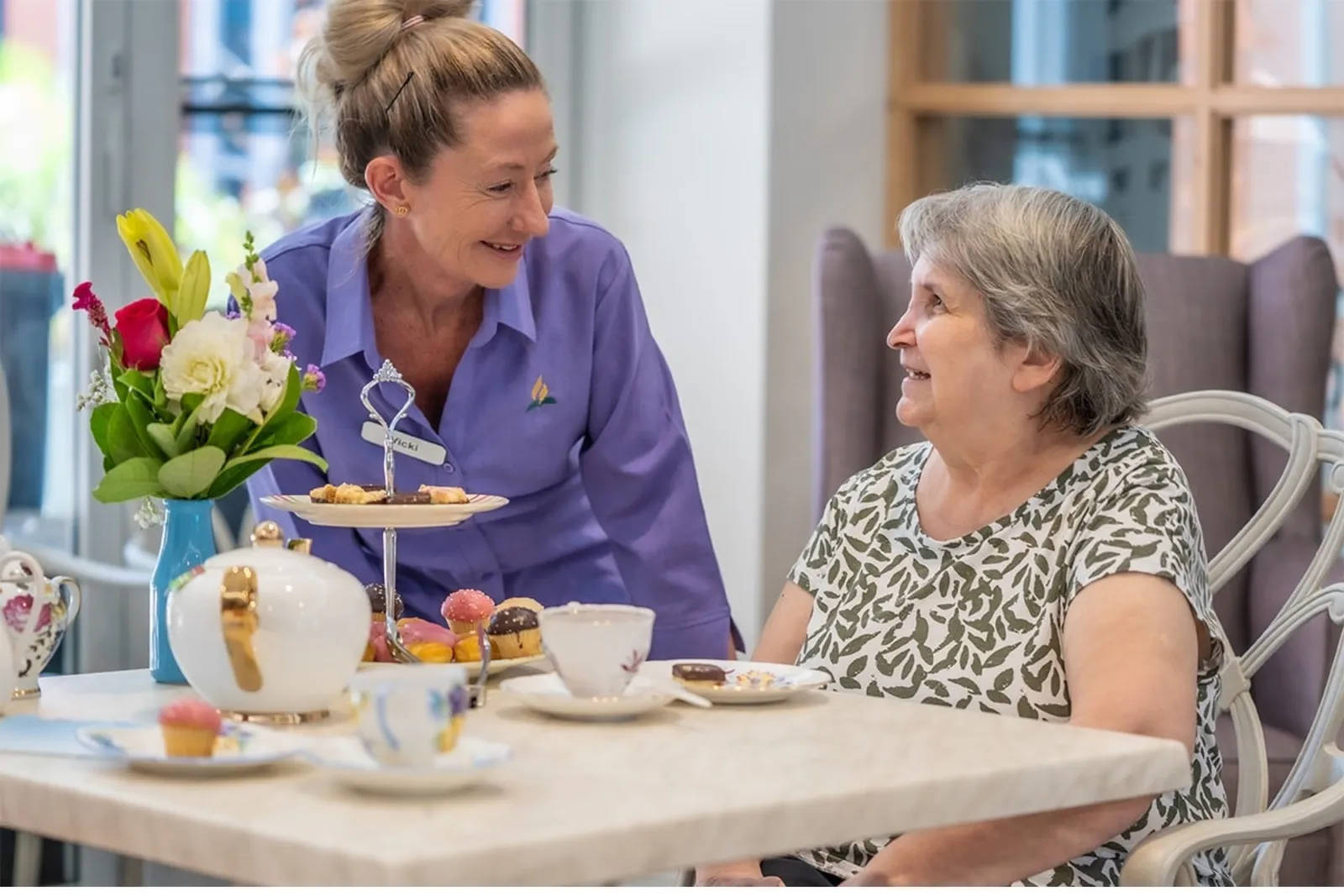 Carer sharing afternoon tea with a smiling aged-care resident