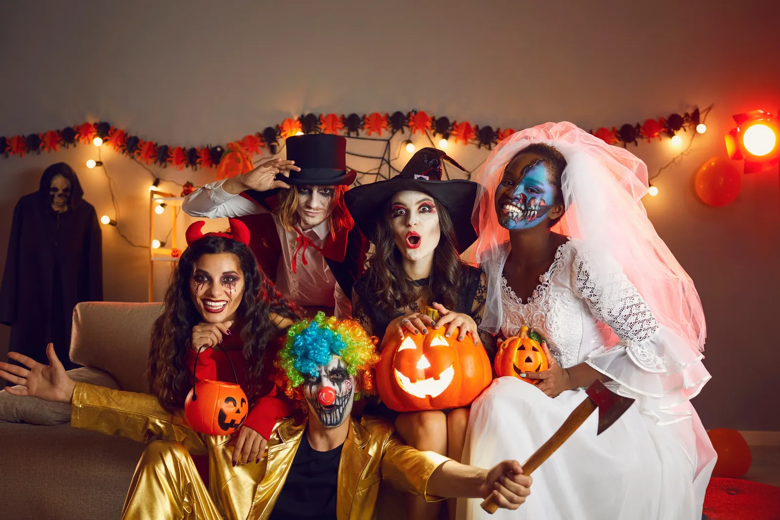 Group of friends in Halloween costumes holding jack-o’-lanterns at a decorated house party