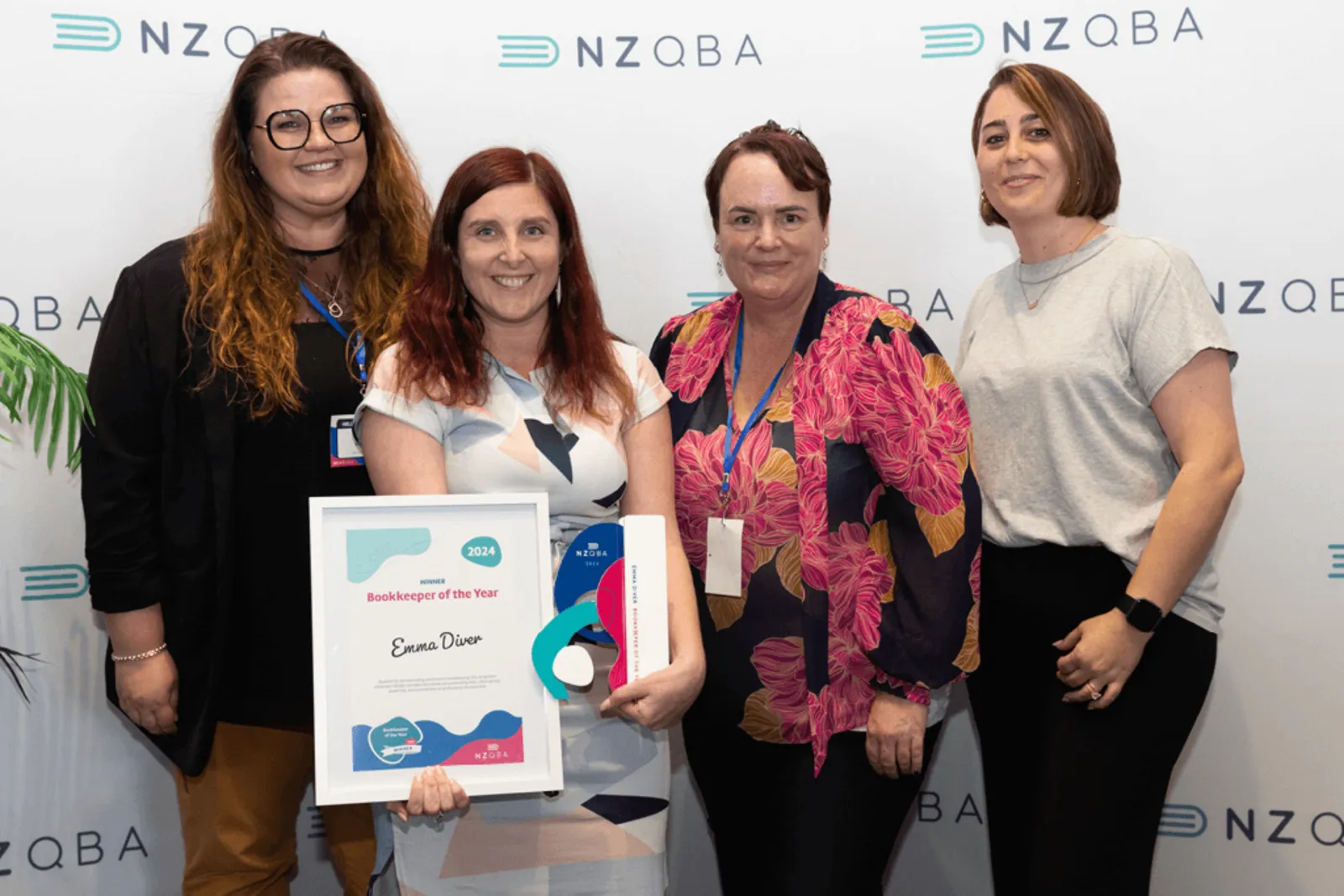 NZQBA members celebrating a Bookkeeper of the Year award in front of an NZQBA media wall
